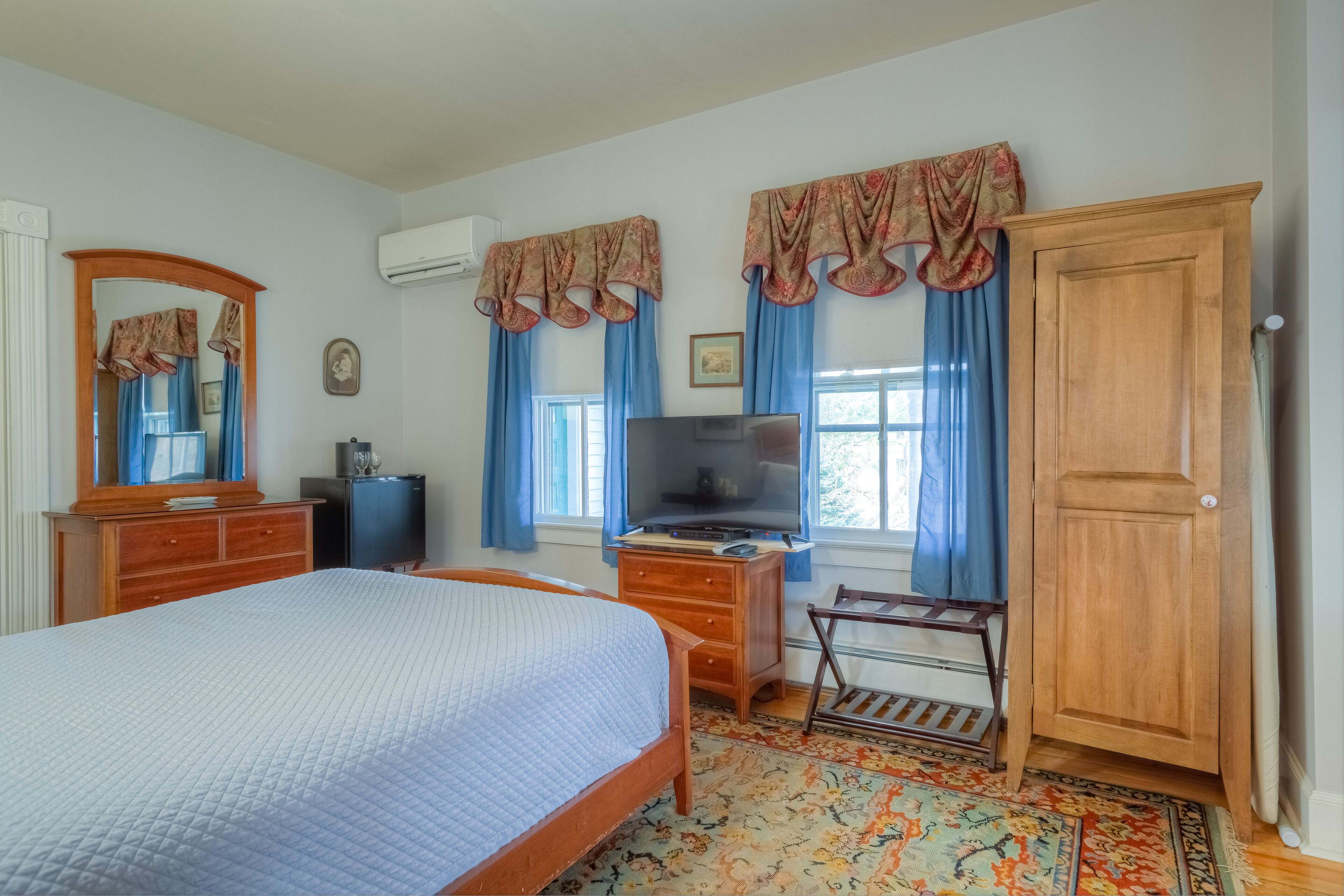 A bedroom with a bed, dresser, vanity, television, and a wardrobe.