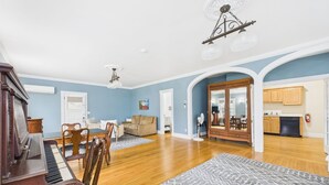 A spacious living room with a piano, a dining area, and a kitchen. - Dodge Cottage (Block Island)