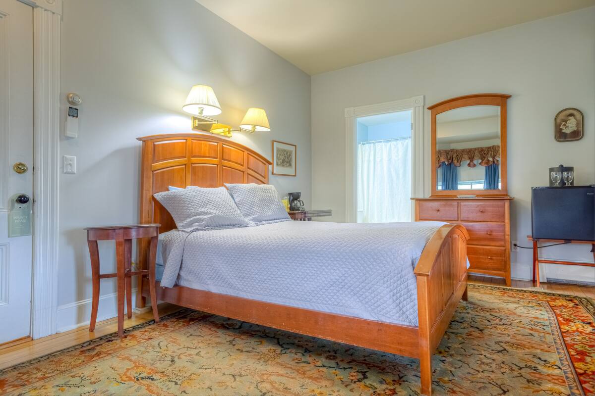 Un dormitorio con cama de madera, lámparas de noche, cómoda, espejo y alfombra estampada.