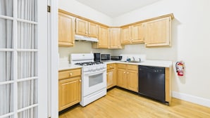 A kitchen with wooden cabinets, a stove, microwave, dishwasher, and a fire extinguisher. - Dodge Cottage (Block Island)
