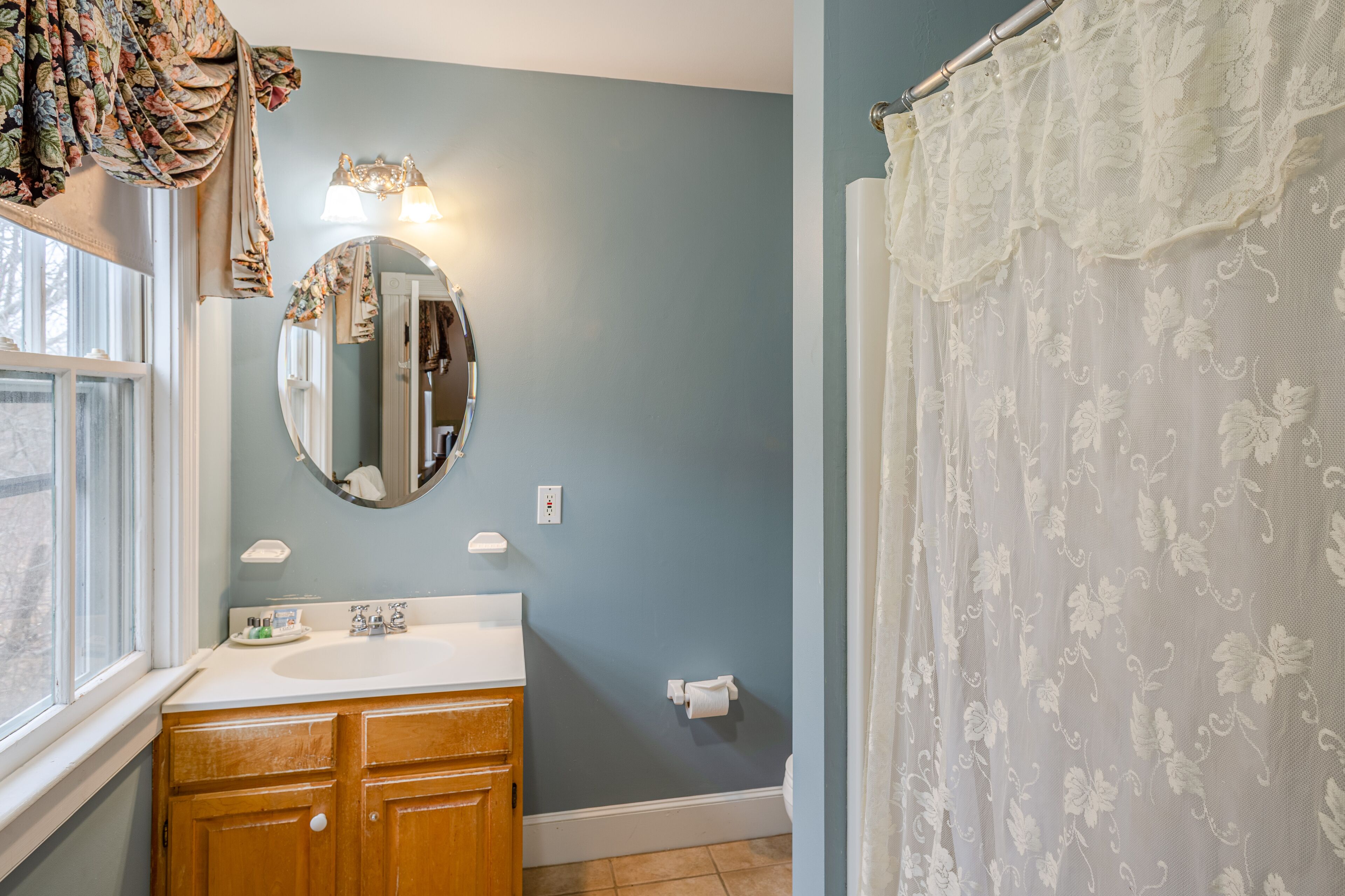 A bathroom with a wooden vanity, a round mirror, a white sink, and a shower curtain with floral patterns.