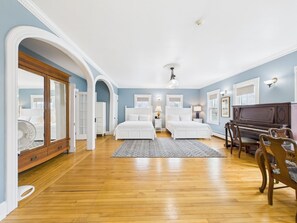 Quarto com duas camas, um piano e um ventilador.