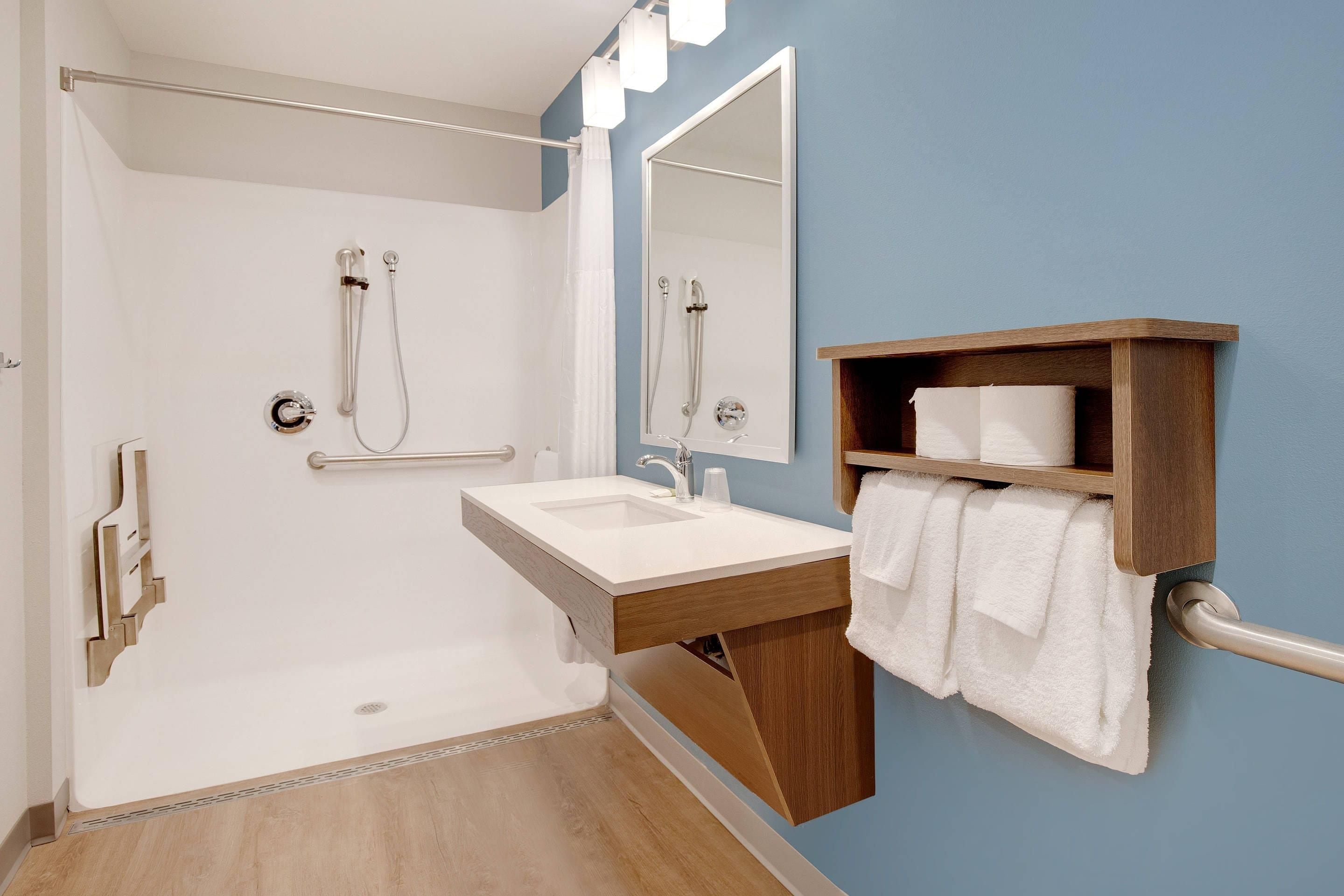 Un baño moderno con ducha a ras de suelo, lavamanos con tocador de madera y espejo.