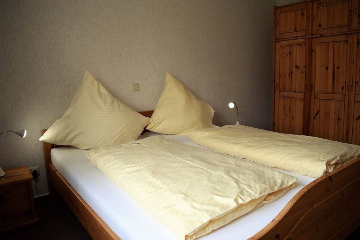 A single bed with two pillows, a bedside table, and a wooden wardrobe.