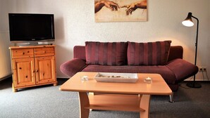 Ett vardagsrum med ett träskåp, en tv, en soffa med randiga kuddar, ett bord med ett bricka fullt med snacks och en tavla på väggen.