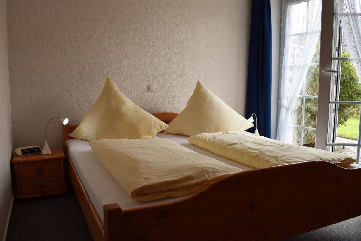 A neatly made bed with two pillows, a bedside table with a lamp, and a window with curtains.