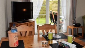 Ett rum med ett träbord, stolar, en tv och ett fönster med gardiner.