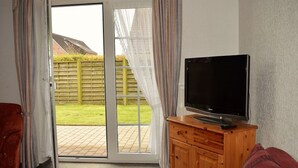 Ett vardagsrum med en tv placerad på ett träskåp, en röd soffa och en skjutdörr i glas som leder ut till en trädgård.