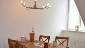 A dining area with a wooden table and chairs, a chandelier, and a bottle of wine on the table. - Haus Uthlande (Dagebuell)