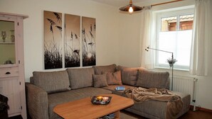 A living room with a sectional sofa, a wooden coffee table, and a window with curtains. - Haus Uthlande (Dagebuell)