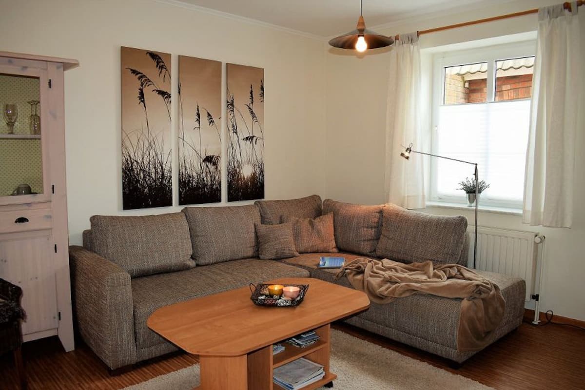 A living room with a sectional sofa, a wooden coffee table, and a window with curtains.