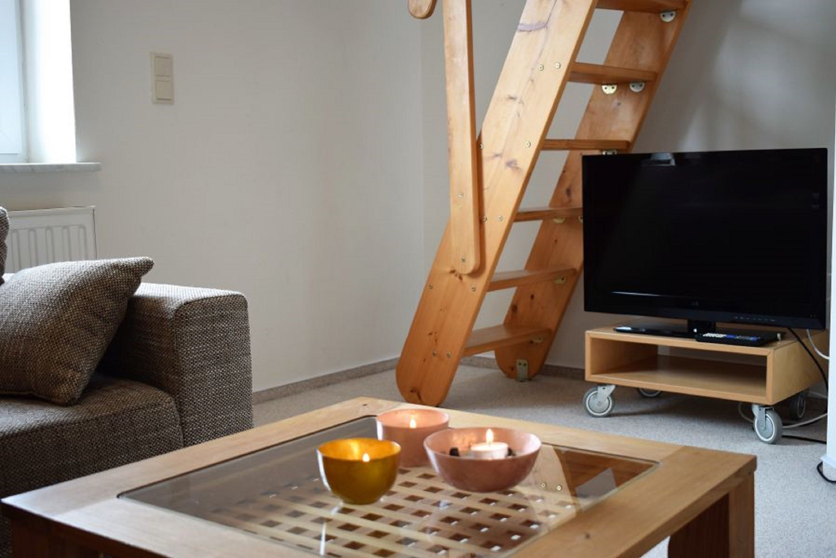 Un salon avec un canapé, une table basse en verre sur laquelle sont posées des bougies, une échelle en bois et un téléviseur sur un meuble.