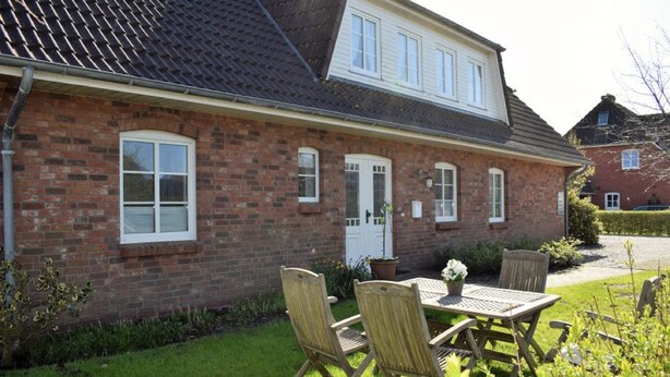 A two-story brick house with a front door, windows, and a small garden with a table and chairs. - Haus Uthlande (Dagebuell)