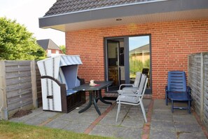 A patio with a table and chairs, a covered grill, and a sliding glass door to a room. - Haus Wattblick (Dagebuell)