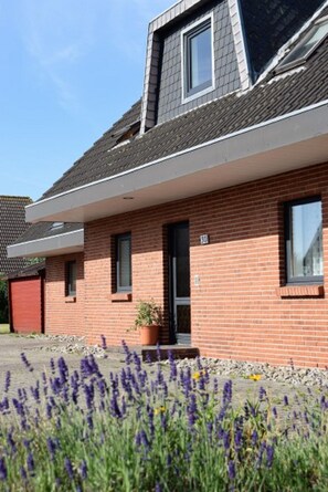 A red brick building with a sloped roof, a small porch, and a potted plant. - Haus Wattblick (Dagebuell)