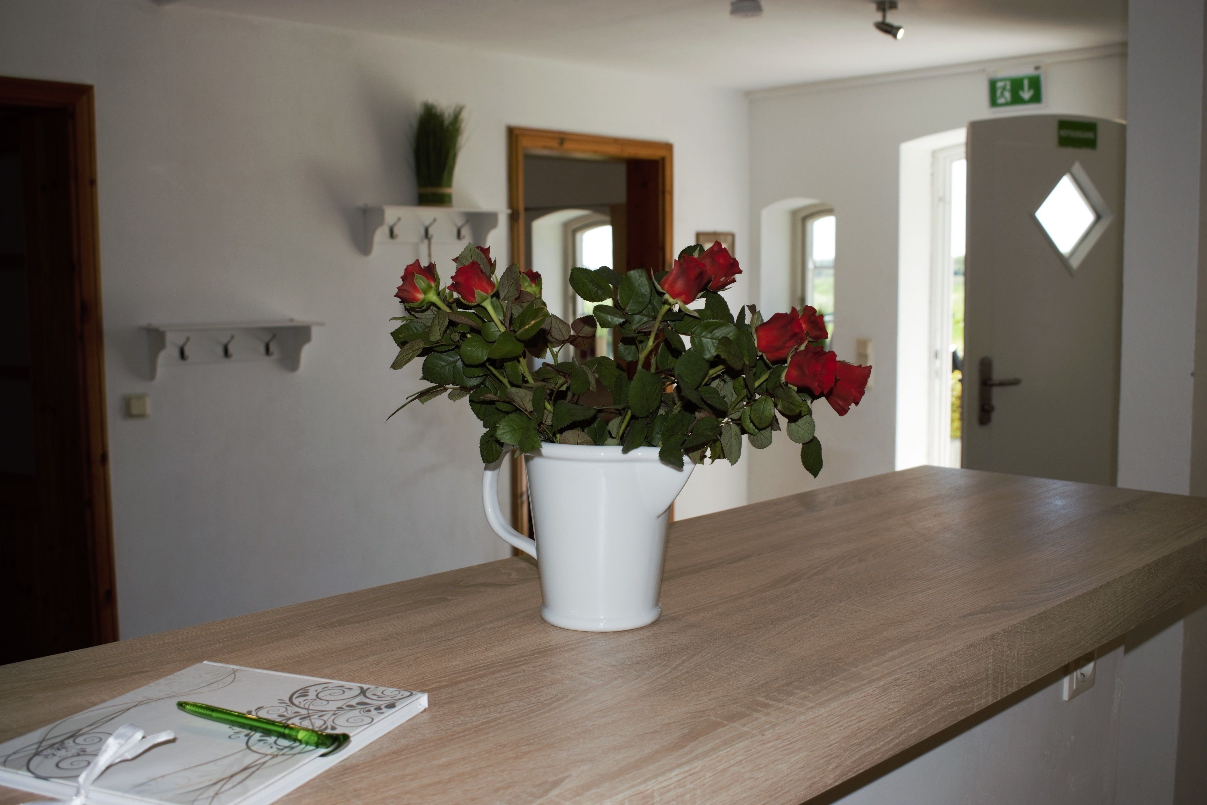 Un jarrón blanco con rosas rojas sobre una encimera de madera en el vestíbulo de un hotel.