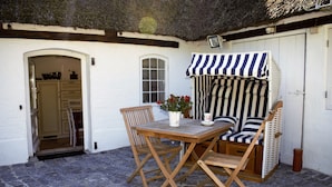 Un patio con una mesa y sillas de madera, un paraguas a rayas y una puerta blanca.