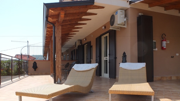 Una terraza con dos sillones de mimbre, una pérgola de madera, un equipo de aire acondicionado y un extintor.