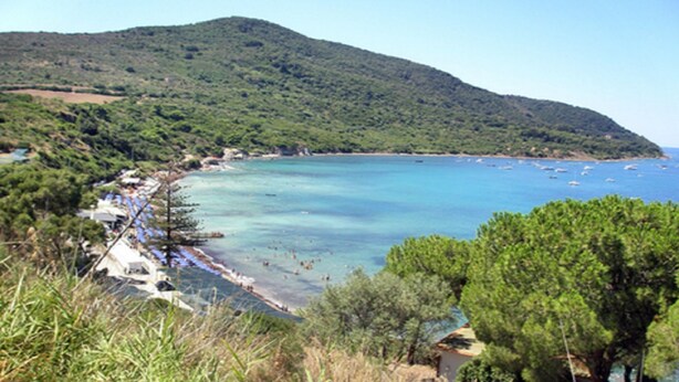 Une zone côtière avec une plage, des bateaux et une chaîne de montagnes en arrière-plan.