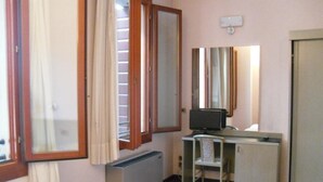 Una habitación pequeña y funcional con cama, escritorio con computadora, silla y radiador.