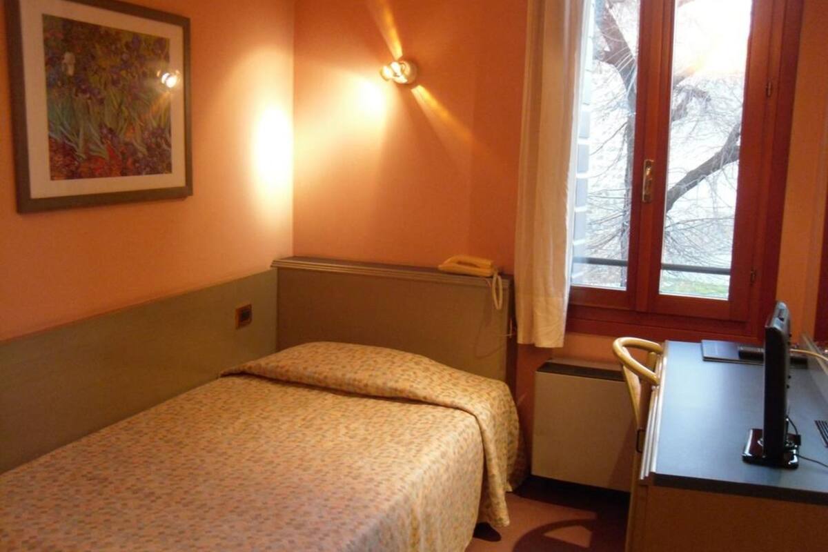 A small, single-bed room with a desk and chair, a radiator, and a window with curtains.