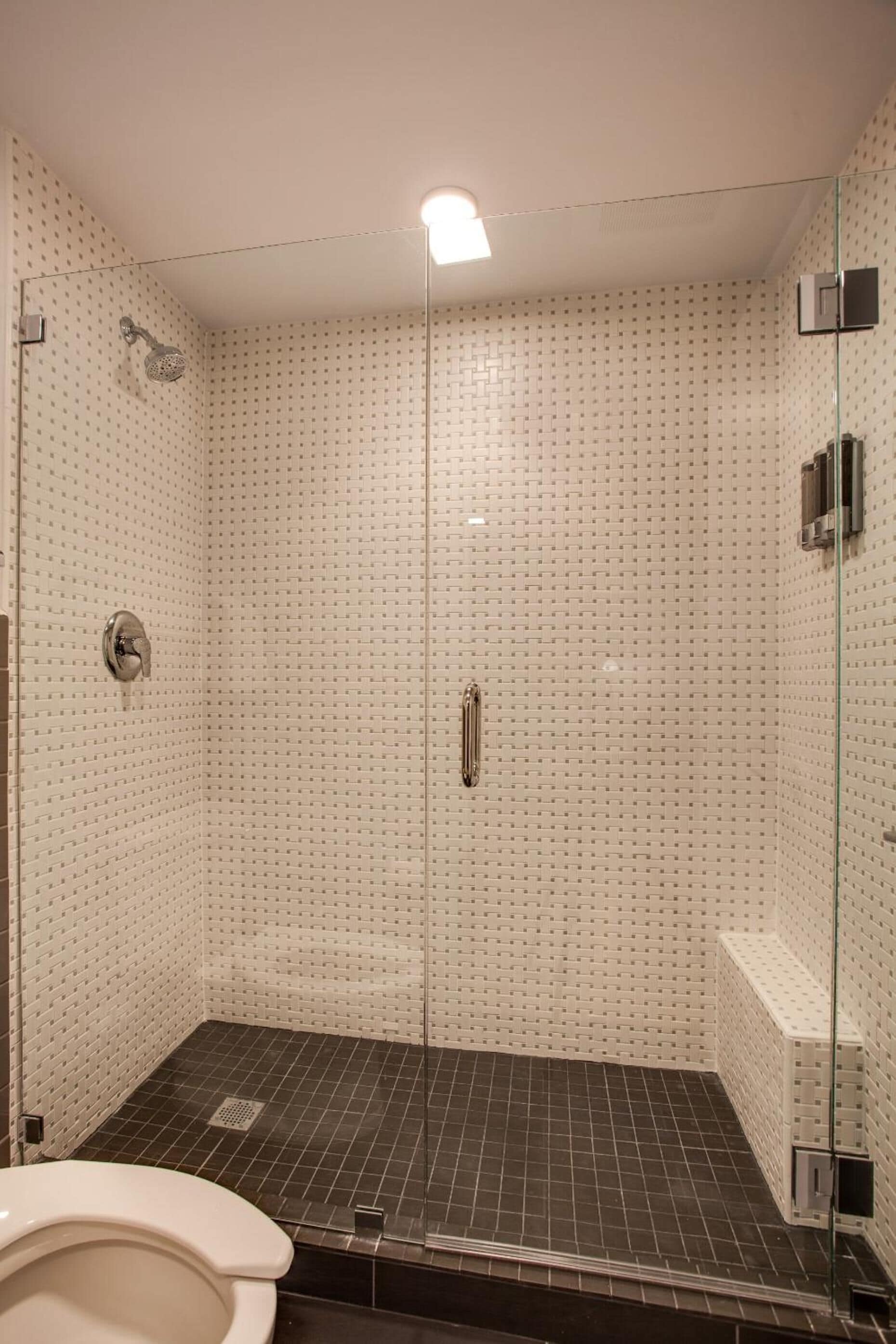 A walk-in shower with a glass door, tiled walls, and a black floor.