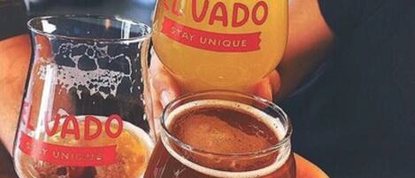 Duas pessoas segurando copos de cerveja El Vado, com uma tatuagem visível em uma das mãos.