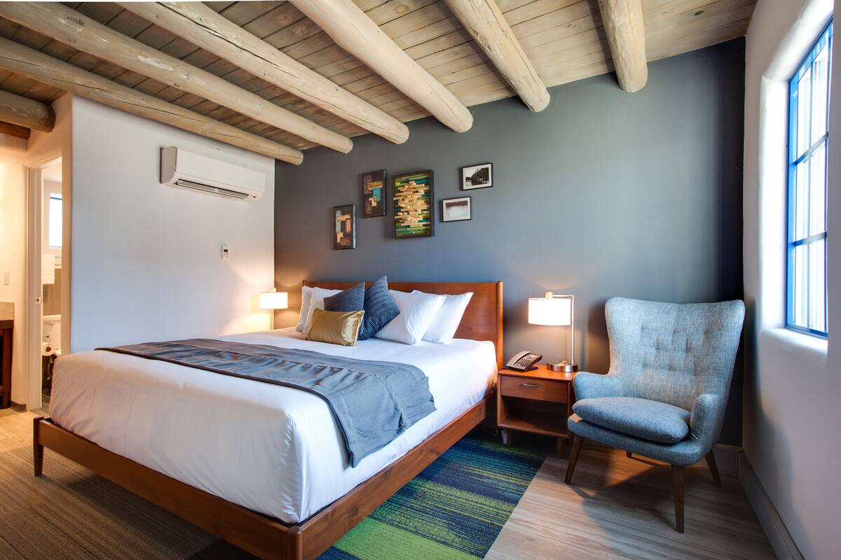 Ein Hotelzimmer mit einem hölzernen Bett, einem blauen Sessel, einem Nachttisch mit Lampe und Bildern an der Wand.