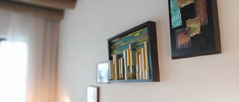 Ein Zimmer mit Bücherregal, einem gerahmten abstrakten Gemälde und einem kleinen Bild an der Wand.