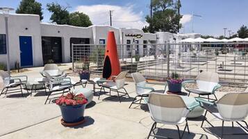 An outdoor seating area with chairs and planters, a distinctive orange sculpture, and a building with a blue door in the background.
