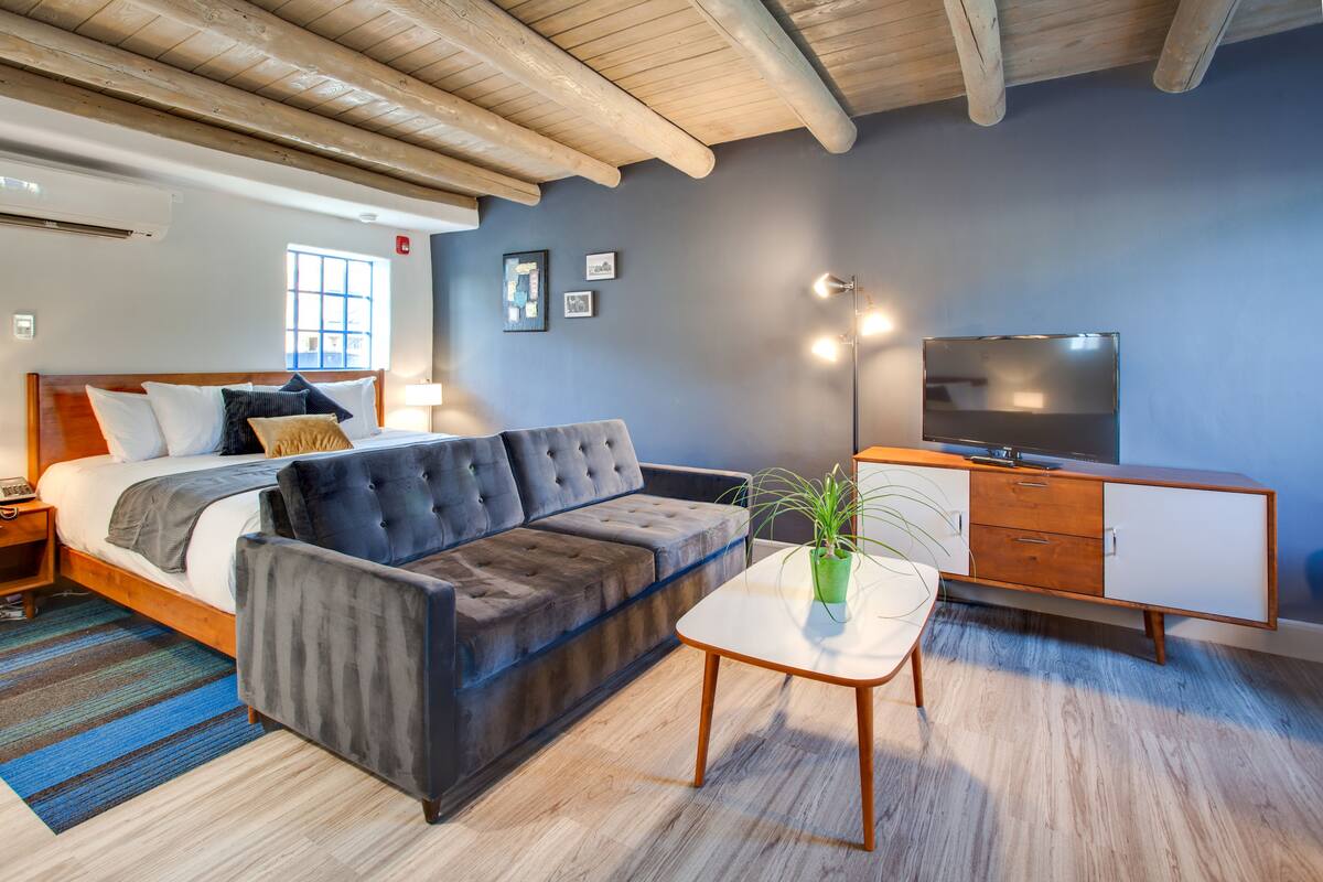 Ein modernes Schlafzimmer mit Bett, Sofa, Nachttisch, Fernseher und einer Topfpflanze.