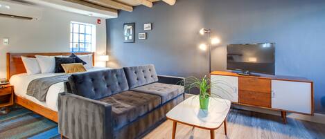 A modern bedroom with a bed, sofa, bedside table, TV, and a potted plant.