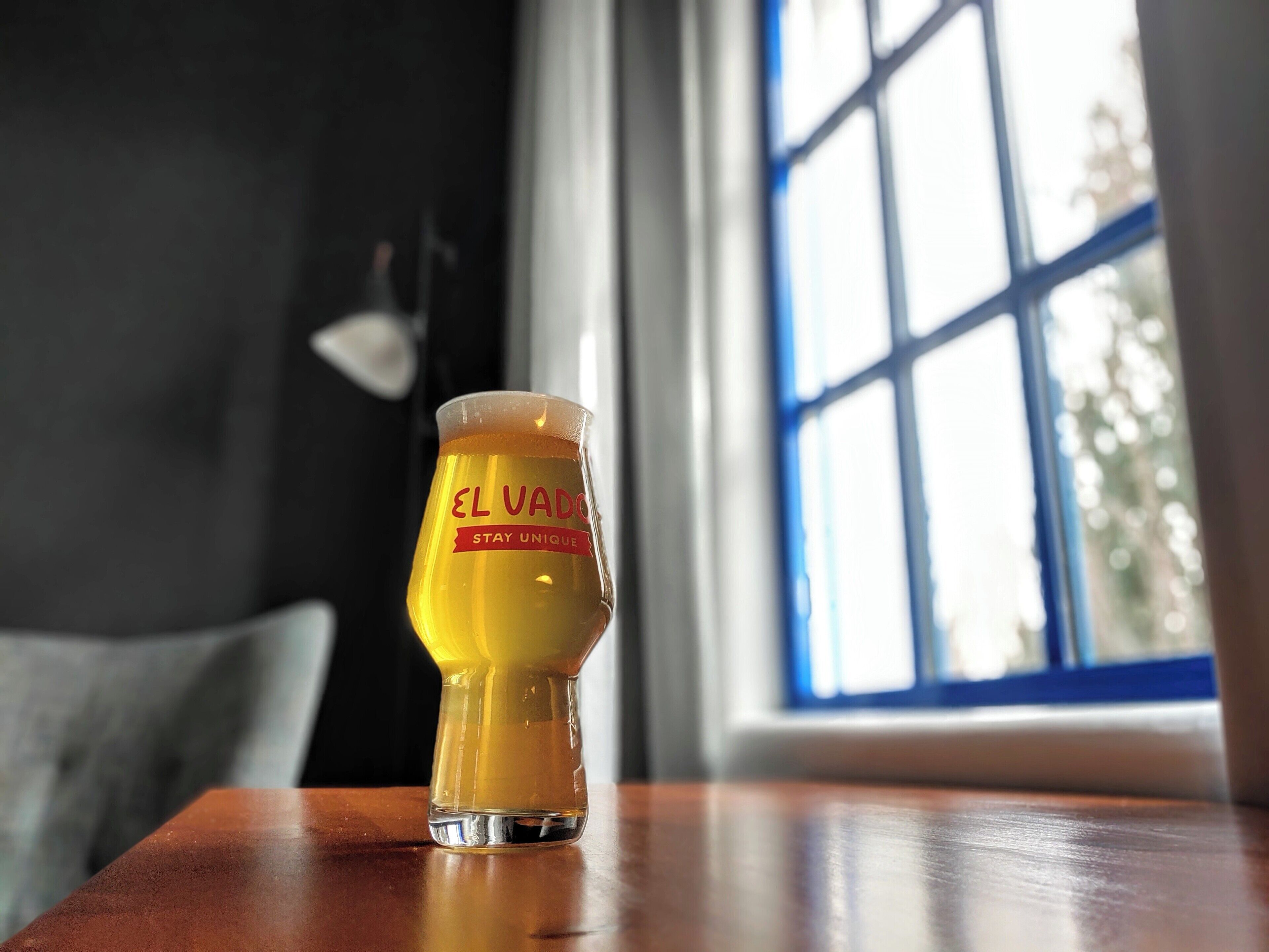 Un got de cervesa sobre una taula de fusta amb una finestra de fons.