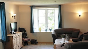 A living room with a sofa, a television, a window with curtains, and a tiled floor. - Haus Frieda (Risum-Lindholm)