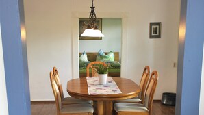 A dining area with a round wooden table, four wooden chairs, a floral tablecloth, and a potted plant. - Haus Frieda (Risum-Lindholm)