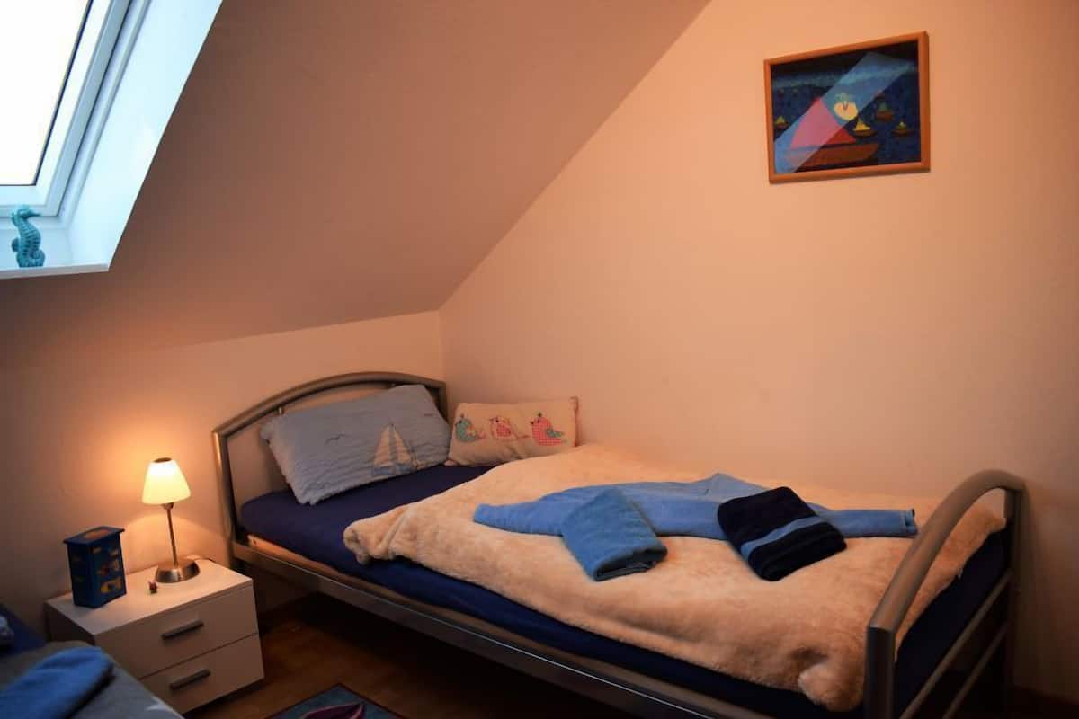 A bedroom with a bed, a nightstand, a lamp, a painting on the wall, and a window.