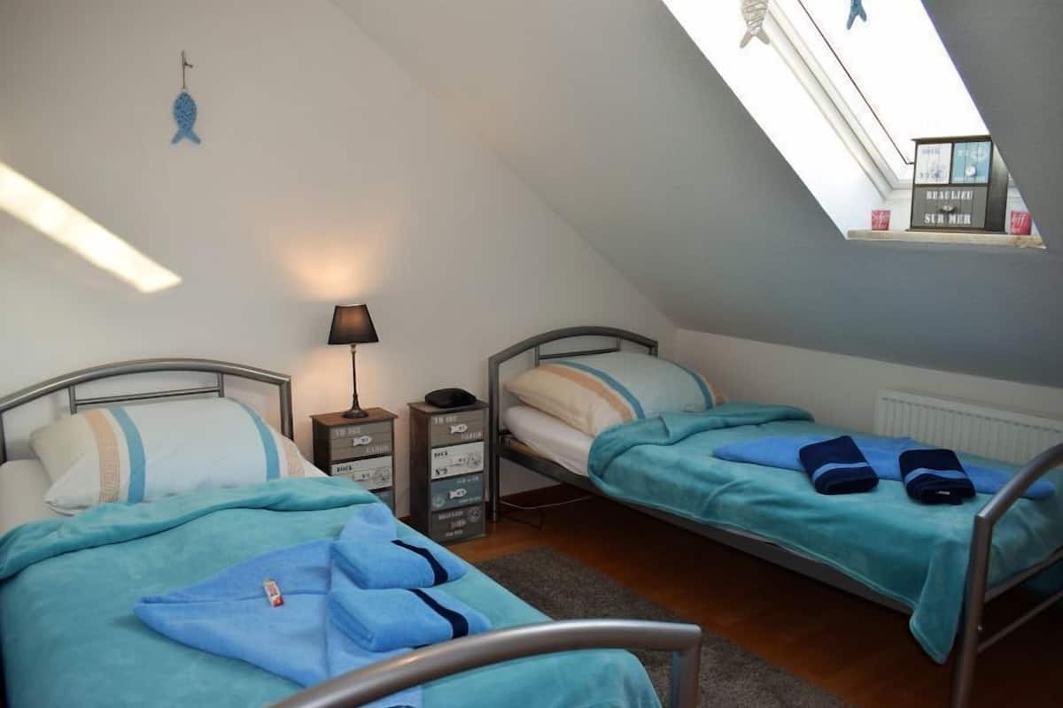 A dormitory room with two beds, a desk, a lamp, and a window with a view of a cityscape.
