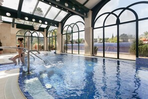 An indoor swimming pool with clear glass walls, a tiled floor, and a person in a swimsuit. - La Sella Premium Lifestyle Apartments (Denia)
