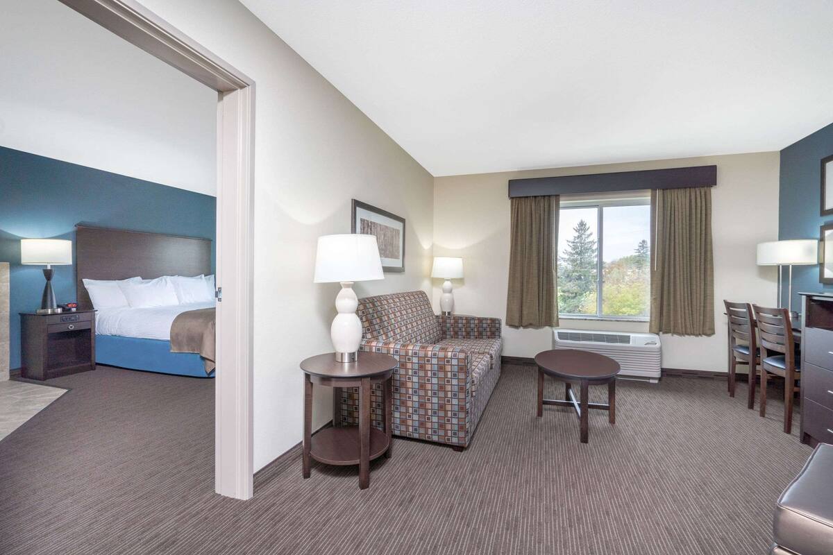 A hotel room with a bed, a sofa, two side tables, a desk, and a chair.