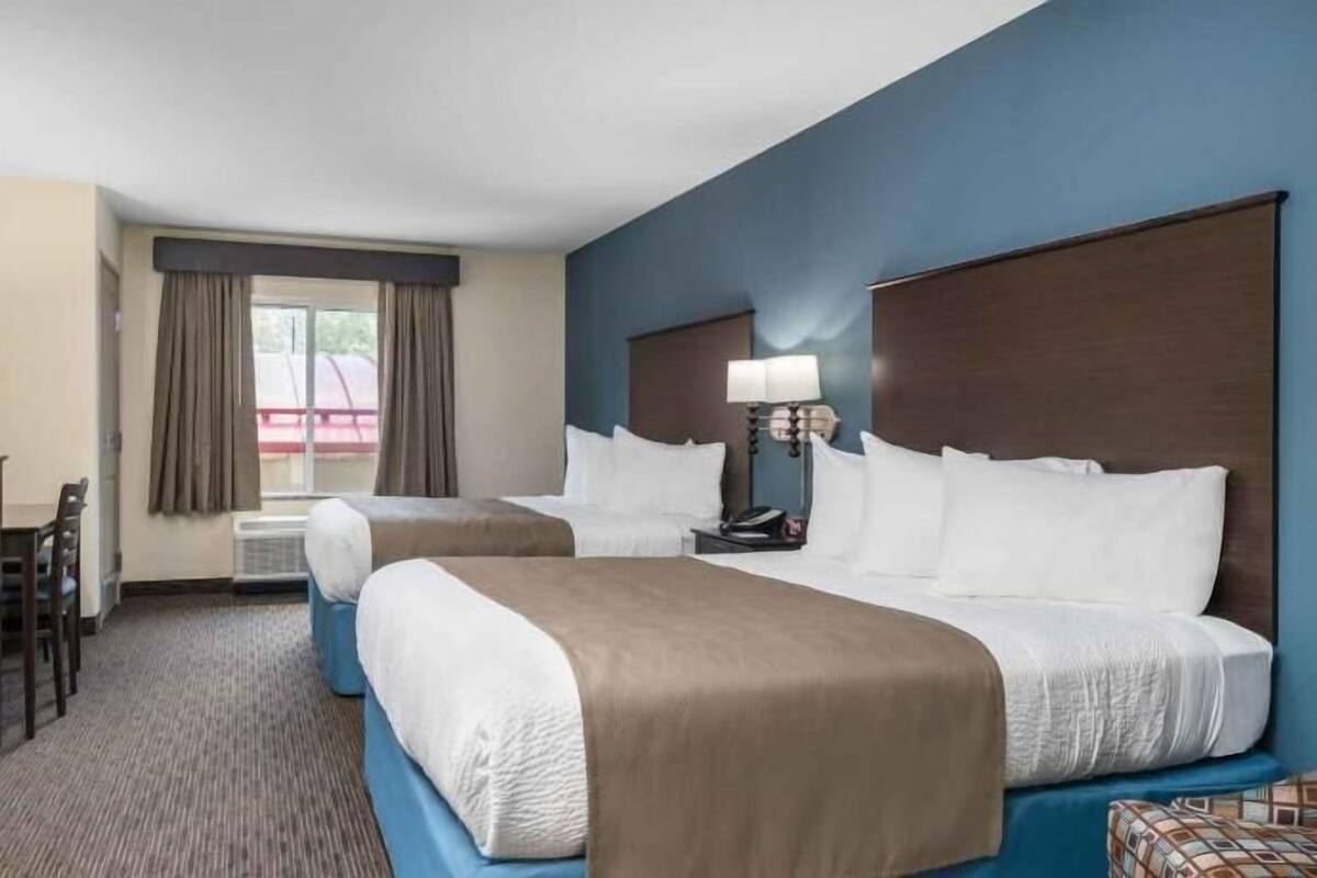 A hotel room with two beds, a desk, a chair, a TV, and a window with curtains.