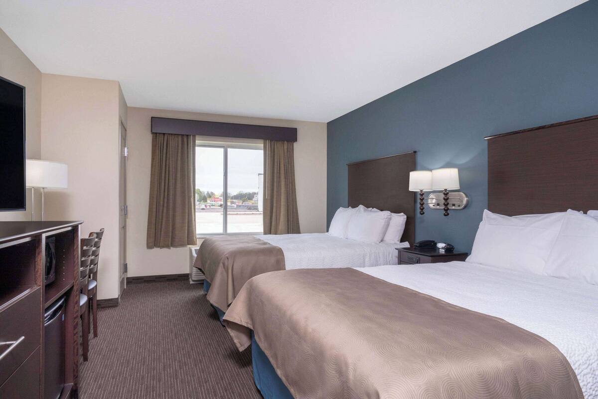A hotel room with two beds, a desk with a television, a window with curtains, and a nightstand with a lamp.
