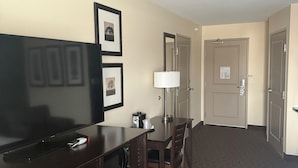 Habitación de hotel con televisor de pantalla plana, escritorio con lámpara, silla y puerta con un número.