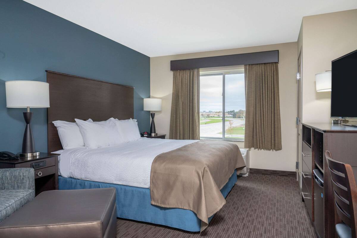 A hotel room with a bed, two bedside lamps, a TV, a desk, and a window with curtains.