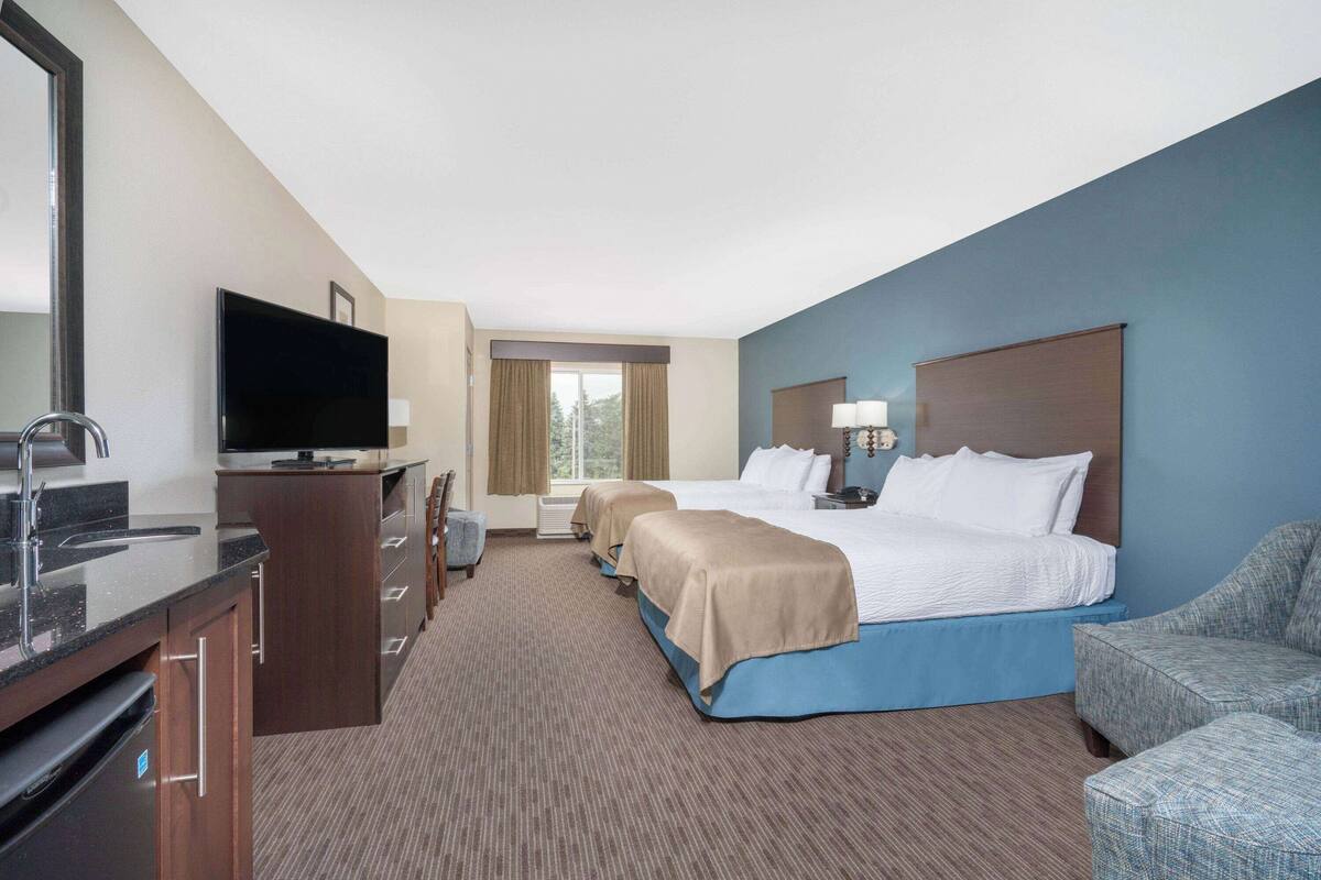 A hotel room with a bed, a TV, a desk with a sink, and a chair.
