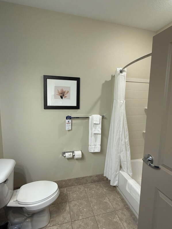 A bathroom with a toilet, a framed picture on the wall, a towel rack with towels, and a shower curtain.