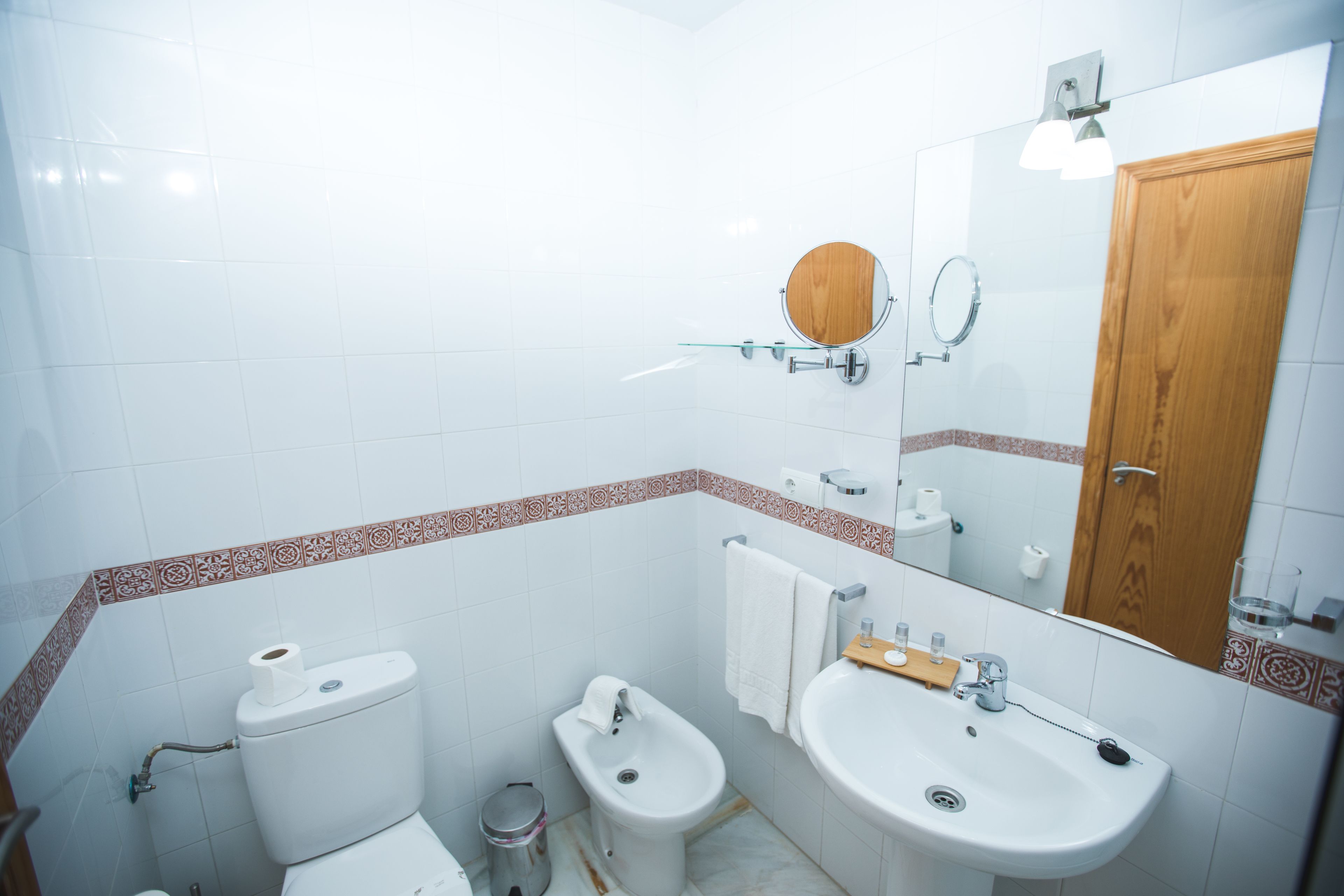 Un baño con inodoro, bidé, lavamanos y espejo.