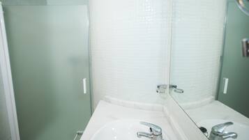 Un baño con lavamanos blanco, espejo y zona de ducha.