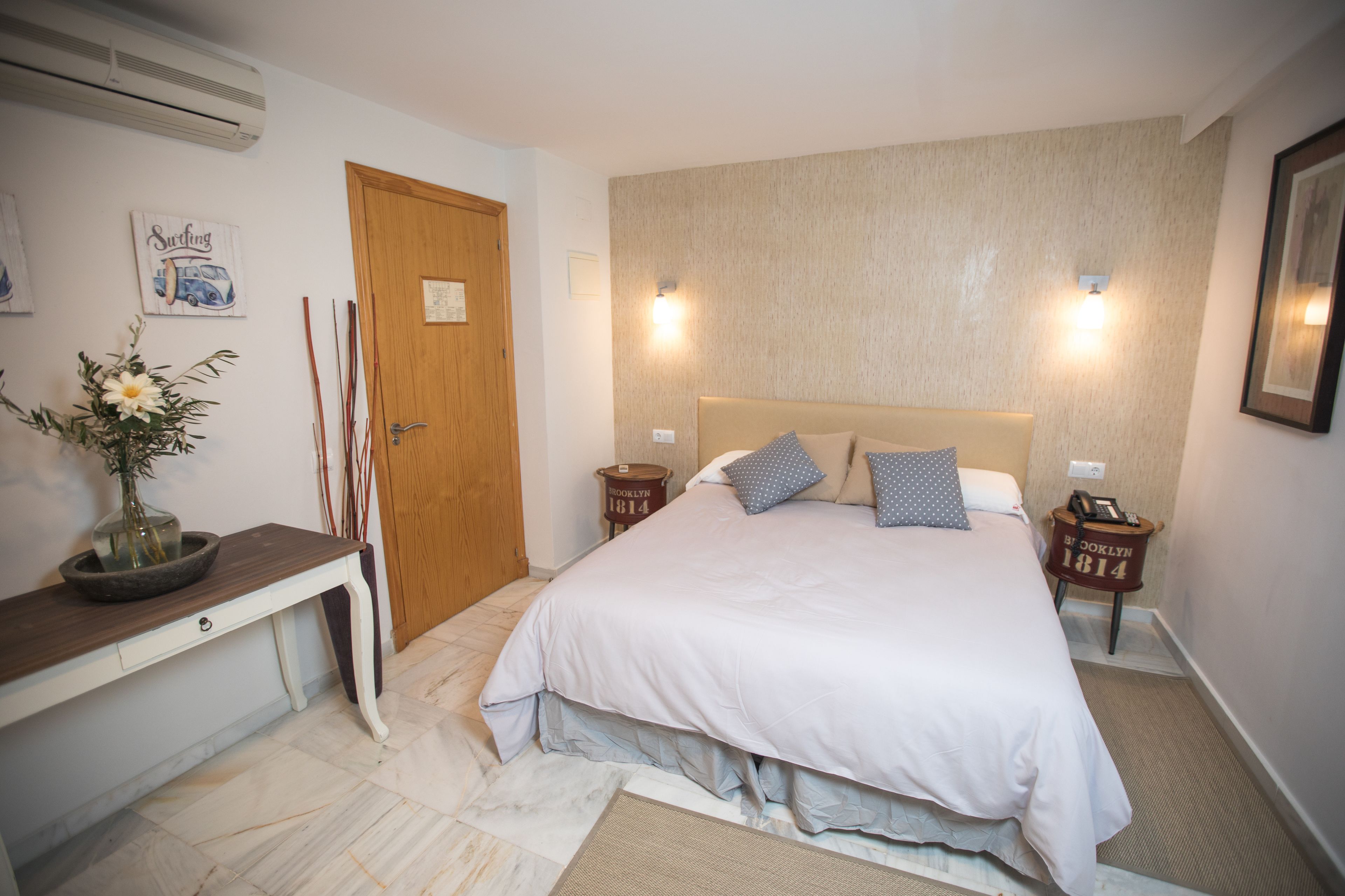A bedroom with a bed, bedside tables, a desk, and a wall-mounted air conditioner.