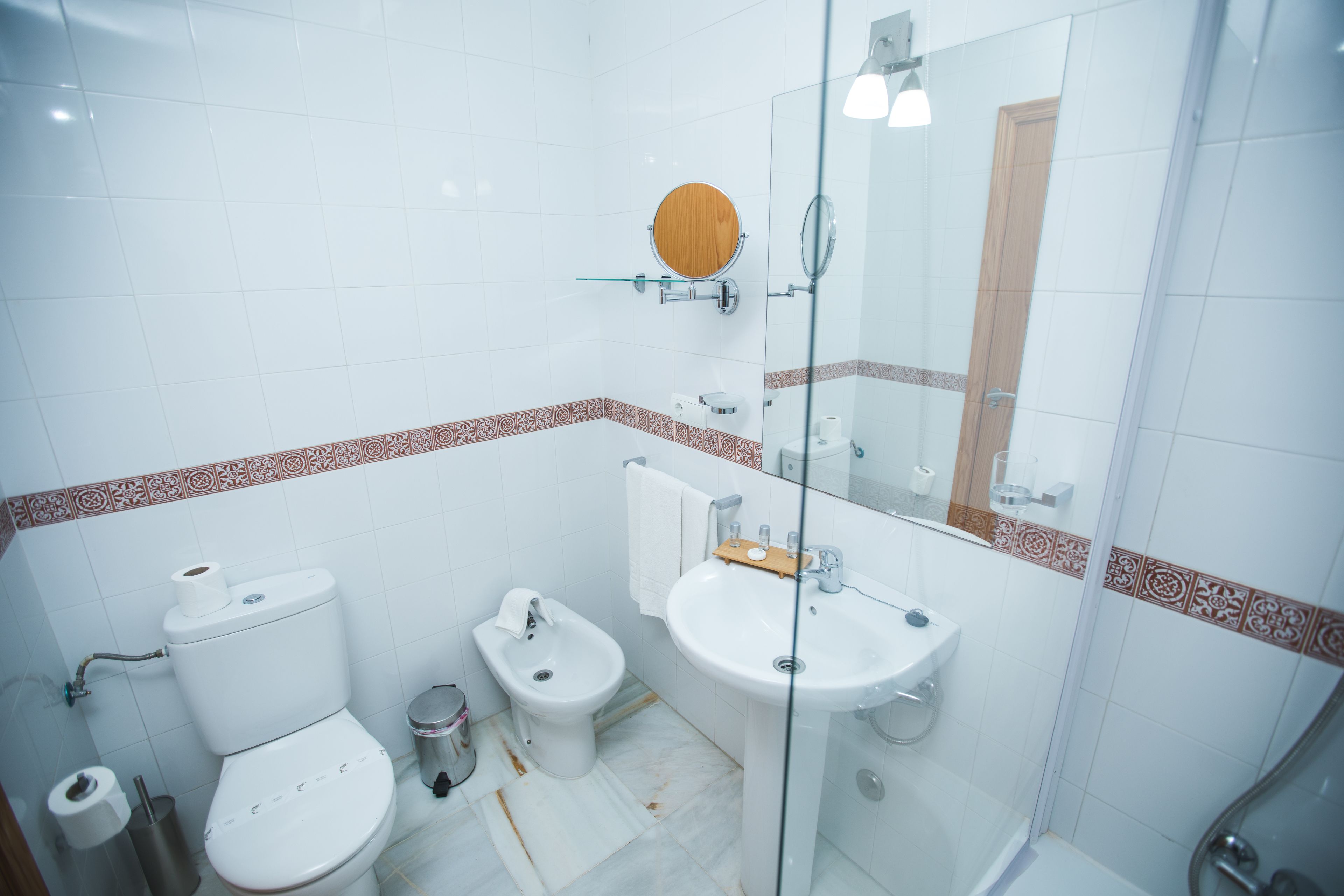 Un baño con inodoro, bidé, lavamanos y cabina de ducha de vidrio.