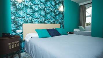 A hotel room with a large bed, a nightstand, a wall with a tropical leaf pattern, and a window with curtains.